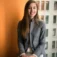 Woman in a gray jacket seated beside a window
